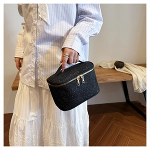 Dettaglio trousse in tweed nero con trama metallica scintillante e doppia zip dorata