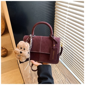 Close-up of burgundy frosted suede handbag featuring white stitching and plush dog charm