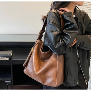Detail view of brown leather hobo bag with stitching and a small zipper pouch accessory
