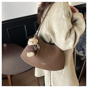 Detailed close-up of brown Hobo shoulder bag with bear pendant on beige wool coat