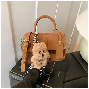 Detailed shot of brown faux leather handbag with a plush puppy charm on art books