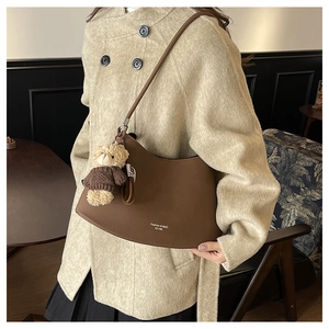 Detail of dark brown leather crescent bag with teddy bear charm and fashion text