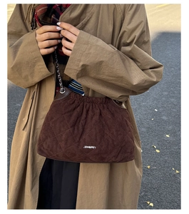 Detailed view of brown quilted suede bucket bag with silver chain strap and metal logo