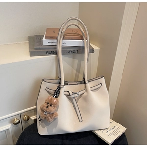 Dettaglio di una borsa tote beige con cinturino decorativo e ciondolo a forma di orsetto