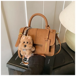 Detail of camel brown crossbody bag with plush dog charm and stylish shoulder strap
