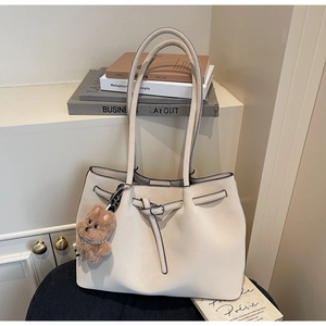 Dettaglio della borsa tote in ecopelle crema con fibbia rotonda e ciondolo orsetto plush