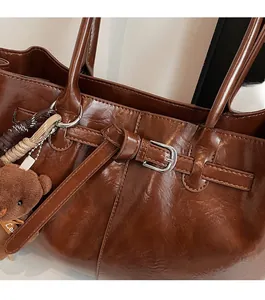 Detail of brown glossy leather tote with adjustable strap, silver buckle and bear charm