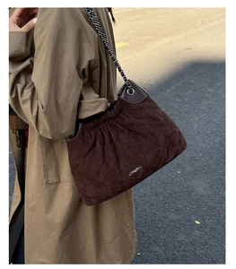 Detail of dark brown quilted crossbody bag with metal chain strap and drawstring closure