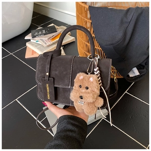 Detail of dark brown matte handbag with contrast stitching and plush dog charm