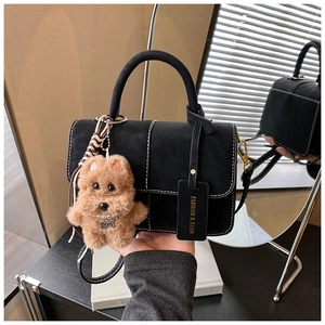 Detail of black suede handbag featuring contrast white stitching and teddy bear charm