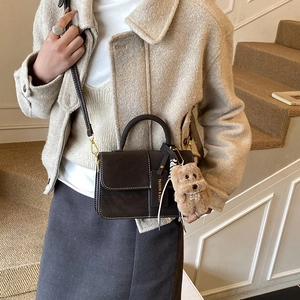 Detail of dark brown matte crossbody bag with white stitching and plush dog pendant