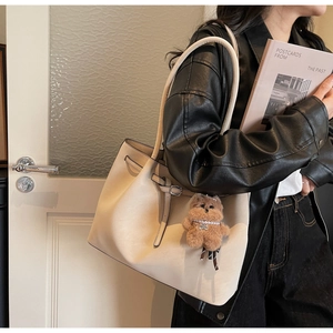 Dettaglio della borsa tote in pelle crema con un orsetto di peluche e texture fine