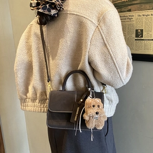 Detail of dark grey suede crossbody bag with contrast stitching and plush dog charm