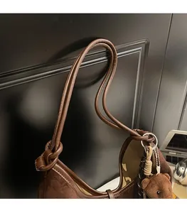 Detail of soft brown suede shoulder bag featuring slim straps and a cute plush bear charm