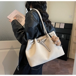 Dettaglio della borsa tote crema con cinturini in pelle e ciondolo orsetto marrone