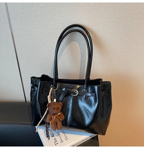 Detail of black faux leather tote bag with decorative buckle and plush bear pendant