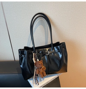 Detail of black faux leather tote bag with decorative buckle and plush bear keychain
