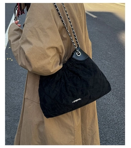 Detail of black quilted bucket bag featuring a chain strap and textured diamond pattern