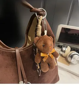 Detail of dark brown plush bear charm with orange bow on suede tote bag