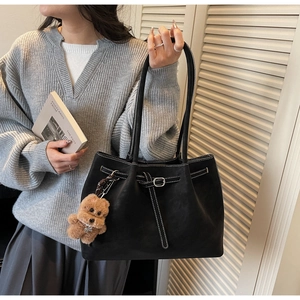 Dettaglio borsa tote in pelle nera con cuciture bianche e ciondolo a forma di orsetto