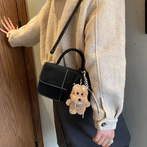 Detail of black faux suede crossbody bag with white stitching and plush dog charm