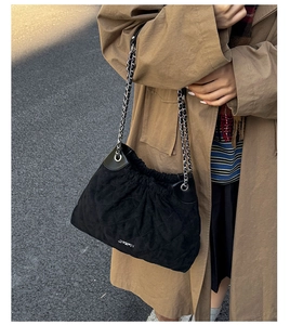 Detail of black quilted chain bucket bag styled with a classic autumn brown trench coat