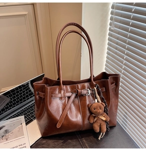 Brown vintage oil-wax leather tote bag detail with decorative buckle and bear charm