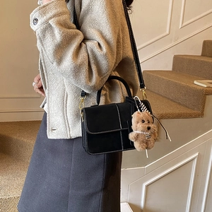 Detail of black crossbody bag with white stitching and plush dog charm on a model