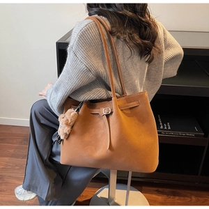Dettaglio della borsa tote in pelle scamosciata marrone con cuciture bianche e orsetto