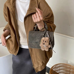 Close-up of a dark grey handbag featuring white stitching and a cute bear charm