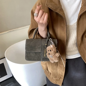 Detail of dark green vintage handbag with white stitching and plush dog charm