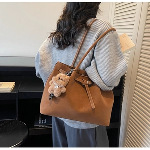 Dettaglio borsa tote in pelle scamosciata marrone con orsetto indossata a spalla da donna