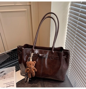 Detail of vintage brown tote bag with fuzzy bear charm on a desk with magazines
