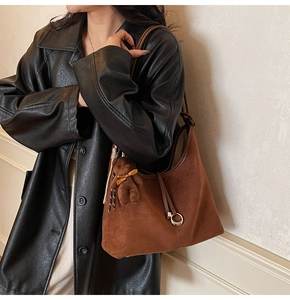 Detail of brown suede tote bag featuring a plush bear pendant and metal ring buckle