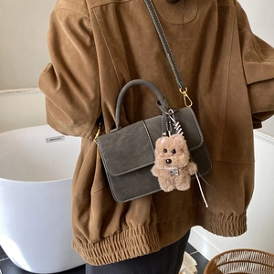 Detail of dark grey crossbody bag with white stitching and plush puppy pendant
