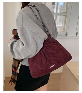 Macro detail of wine red quilted bucket bag with velvet texture and golden chain strap