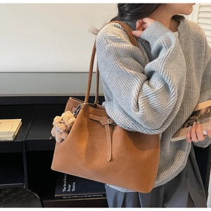 Dettaglio di una grande borsa tote in pelle marrone con ciondolo a orsetto e tracolla