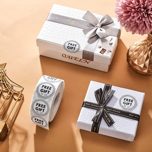Détail d'étiquettes CADEAU GRATUIT rondes sur un coffret cadeau élégant avec ruban et fleurs