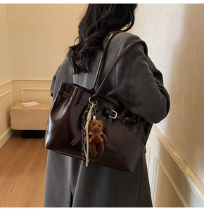 Detail of dark brown tote bag with bear charm and glossy finish on grey coat