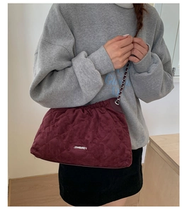 Detail of burgundy quilted crossbody bag showing silver chain strap and logo texture