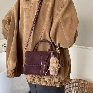 Detail of burgundy crossbody bag with contrast stitching and teddy bear charm on model