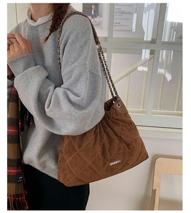 Detail of a brown quilted bucket bag with chain strap and matte suede texture on model