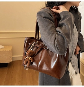 Detail of dark brown tote bag with glossy finish and cute teddy bear charm accessory