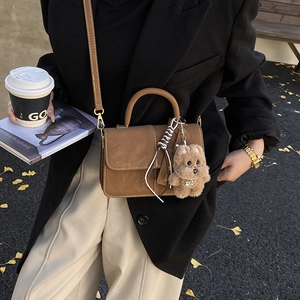 Brown leather crossbody bag detail featuring a cute puppy plush charm and top handle