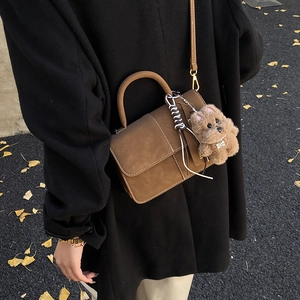 Brown leather crossbody bag with fluffy dog charm shown in autumn leaf setting