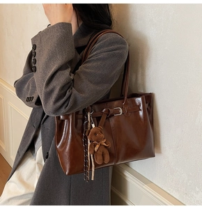 Detail of dark brown wax leather tote bag with metal buckle and teddy bear charm accessory