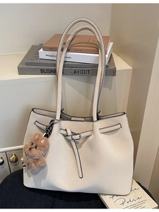 Grande borsa tote beige minimalista con ciondolo a cucciolo su una sedia scura