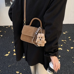 Brown suede crossbody bag detail with plush bear charm and adjustable shoulder strap