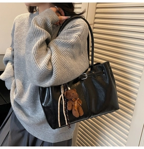 Close-up of black oil-wax leather tote bag with cute bear charm and woven details