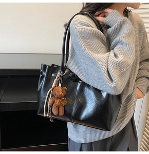 Detail of black matte tote bag with cute brown bear charm and soft knit sweater styling